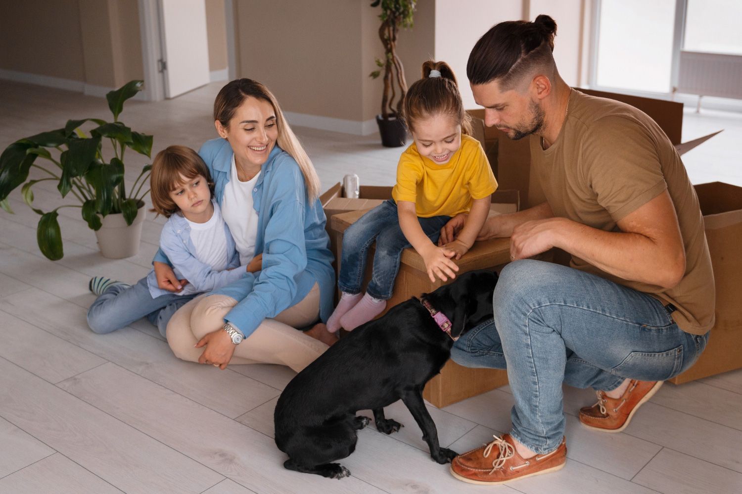 A family is sitting on the floor with boxes and a dog.