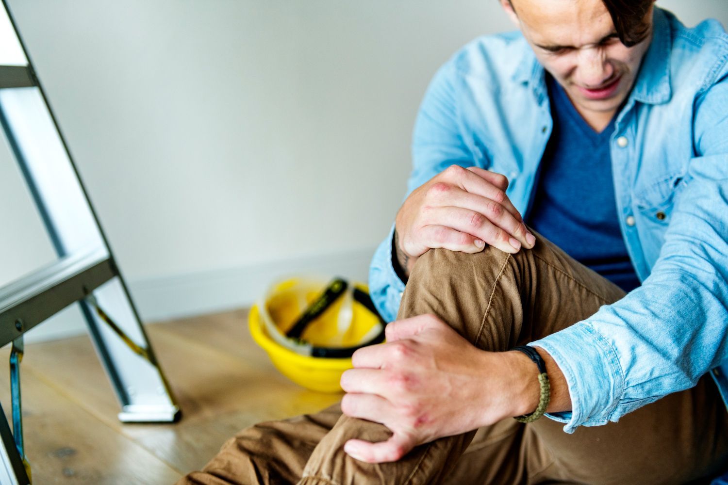 A man is sitting on the floor with his knee in pain.