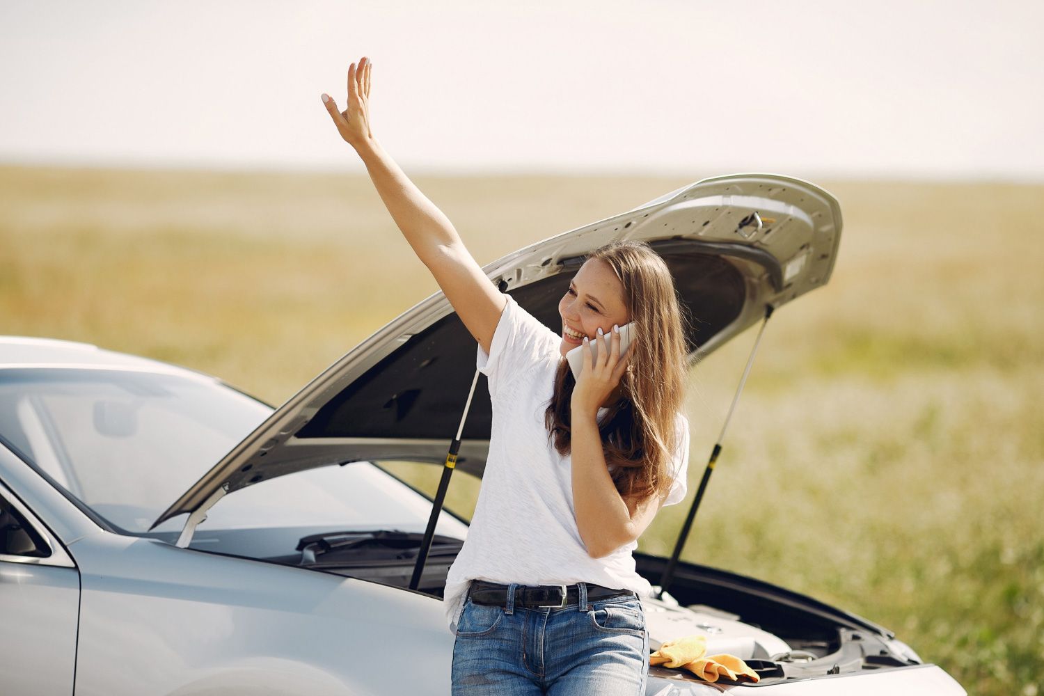 A woman is talking on a cell phone next to a broken down car.