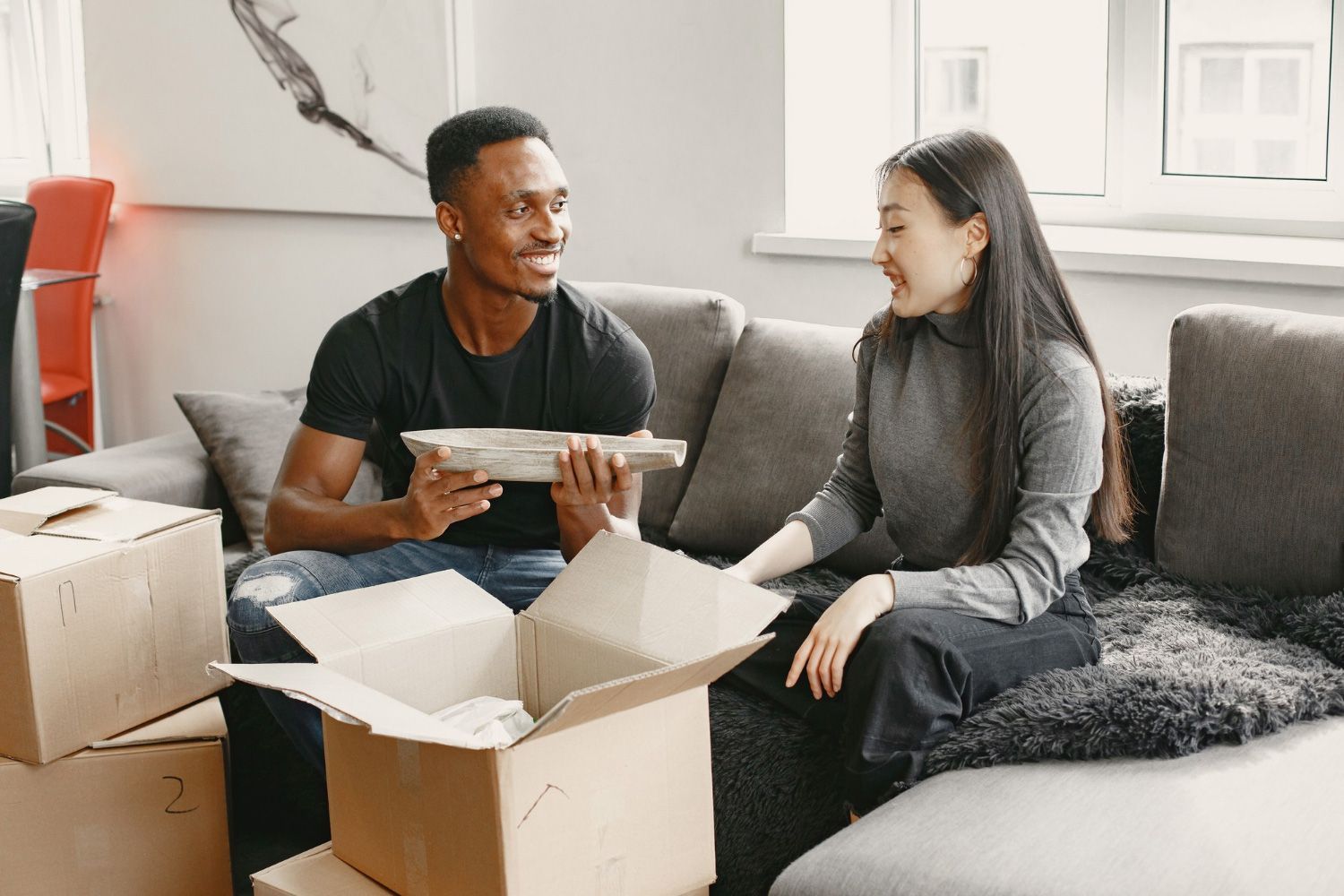 A man and a woman are sitting on a couch with cardboard boxes.