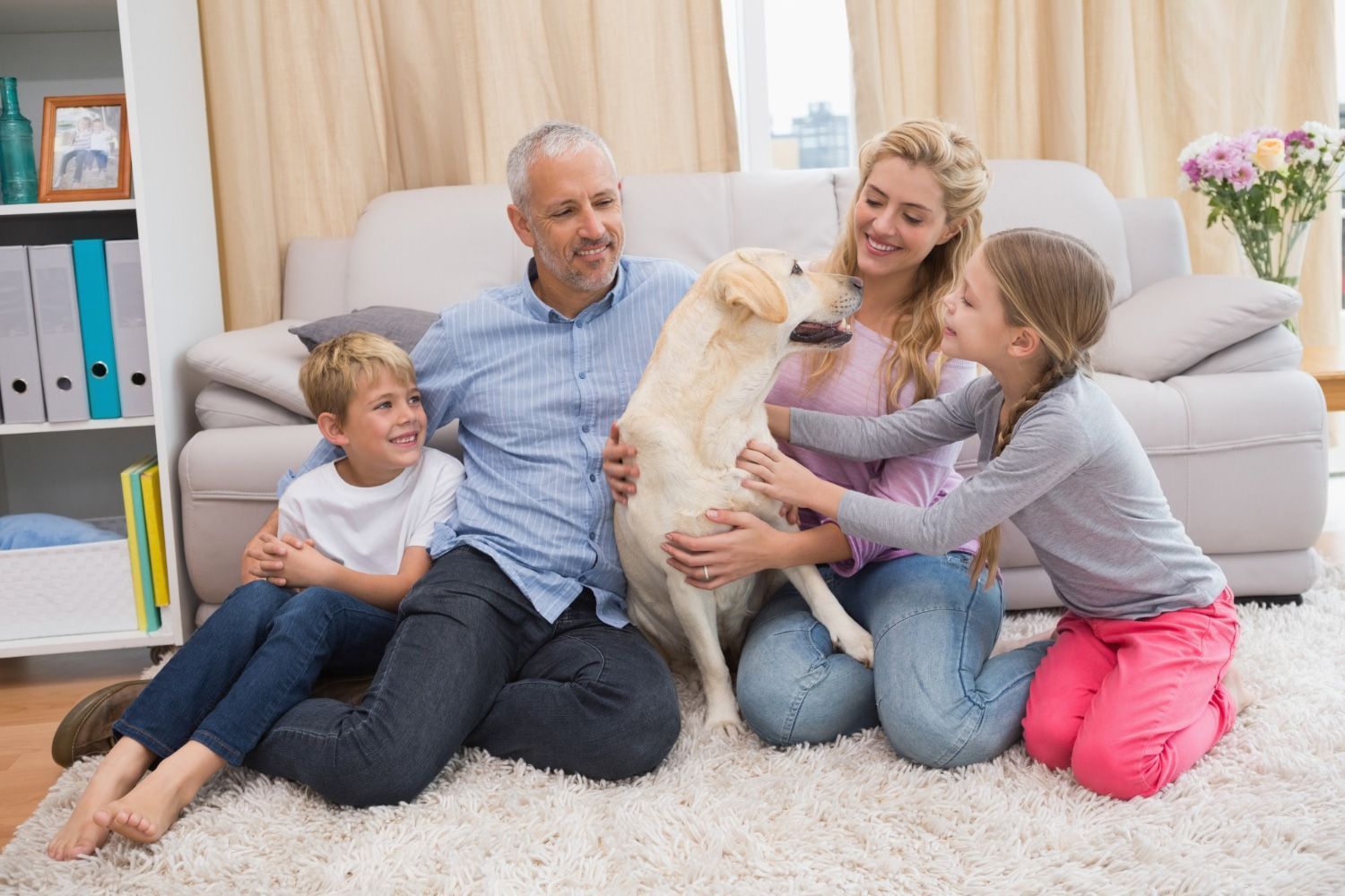 A family is sitting on the floor with a dog in their living room.