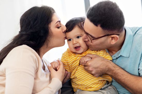 A man and a woman are kissing a baby on the cheek.