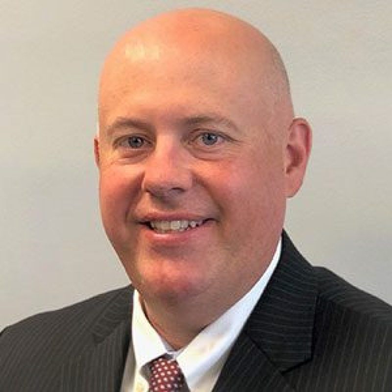 A bald man in a suit and tie is smiling for the camera.