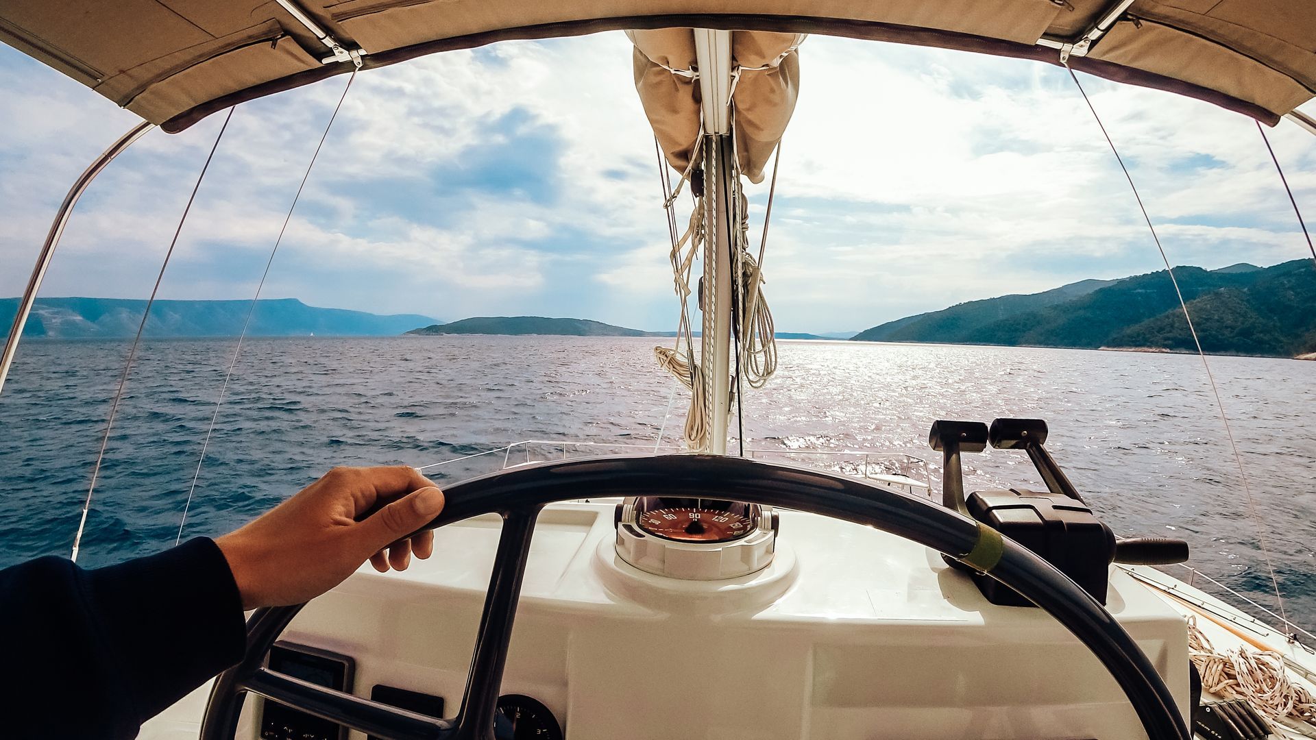 A person is holding the steering wheel of a sailboat in the ocean.