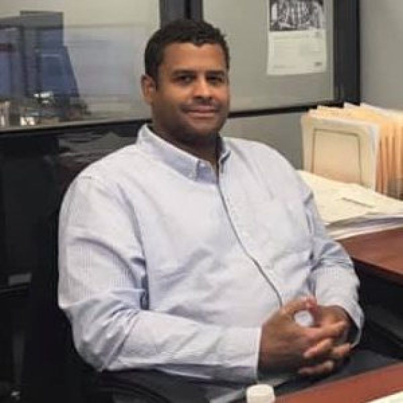 A man in a blue shirt is sitting at a desk in an office.