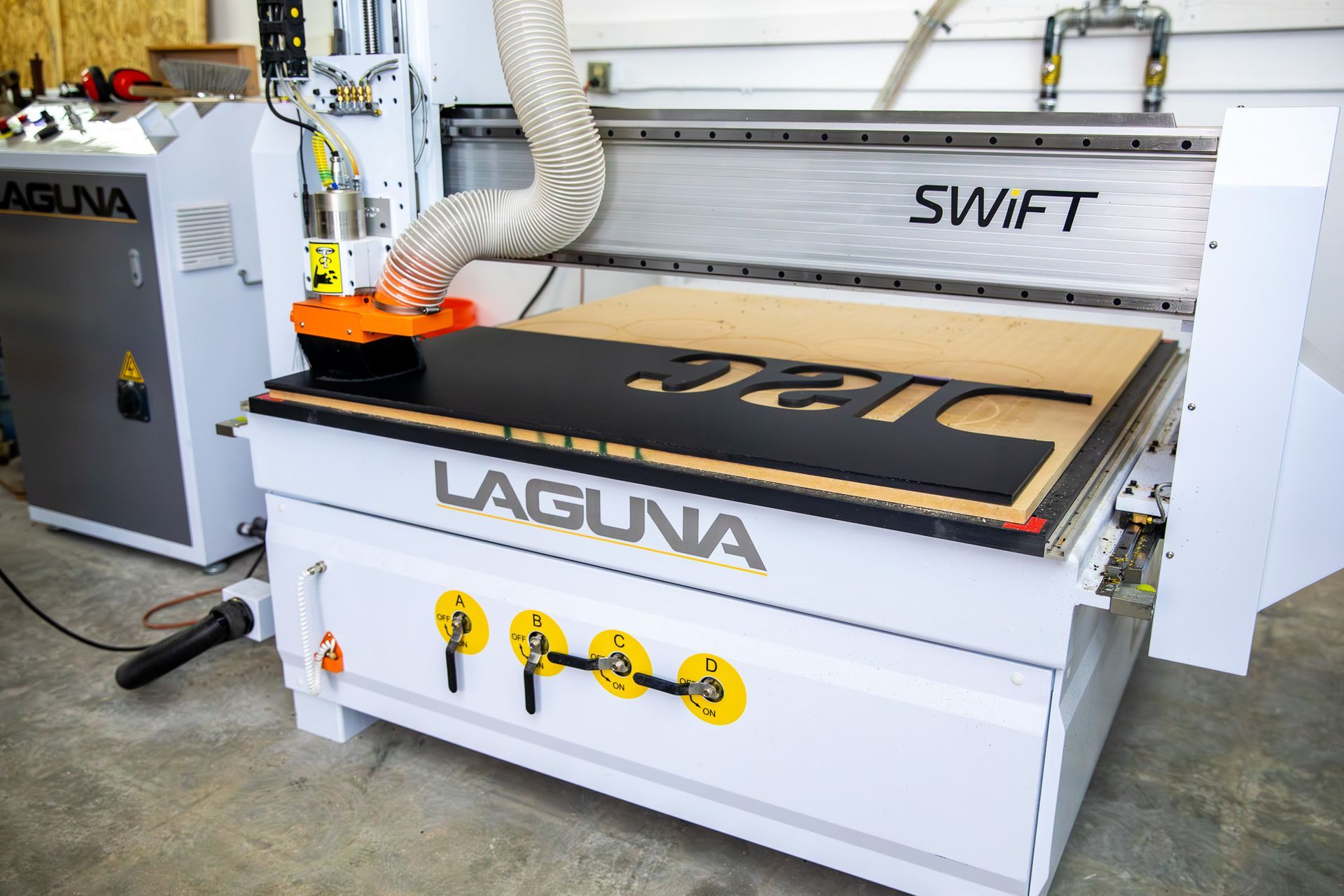 CNC router machine cutting a wooden sheet in a workshop, with a dust hose attached