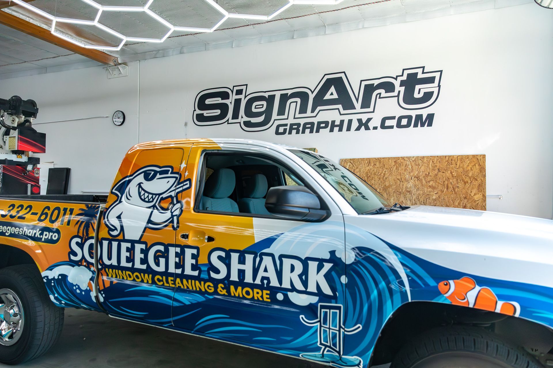 SignArt vehicle wrap with a blue Squeegee Shark truck inside a sign shop