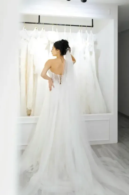 Woman in wedding dress in a boutique, looking at other gowns. White dresses hang in background.