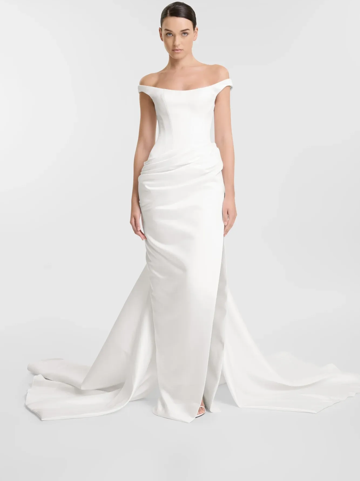 Woman in white off-the-shoulder wedding gown, standing in a studio with a long train.