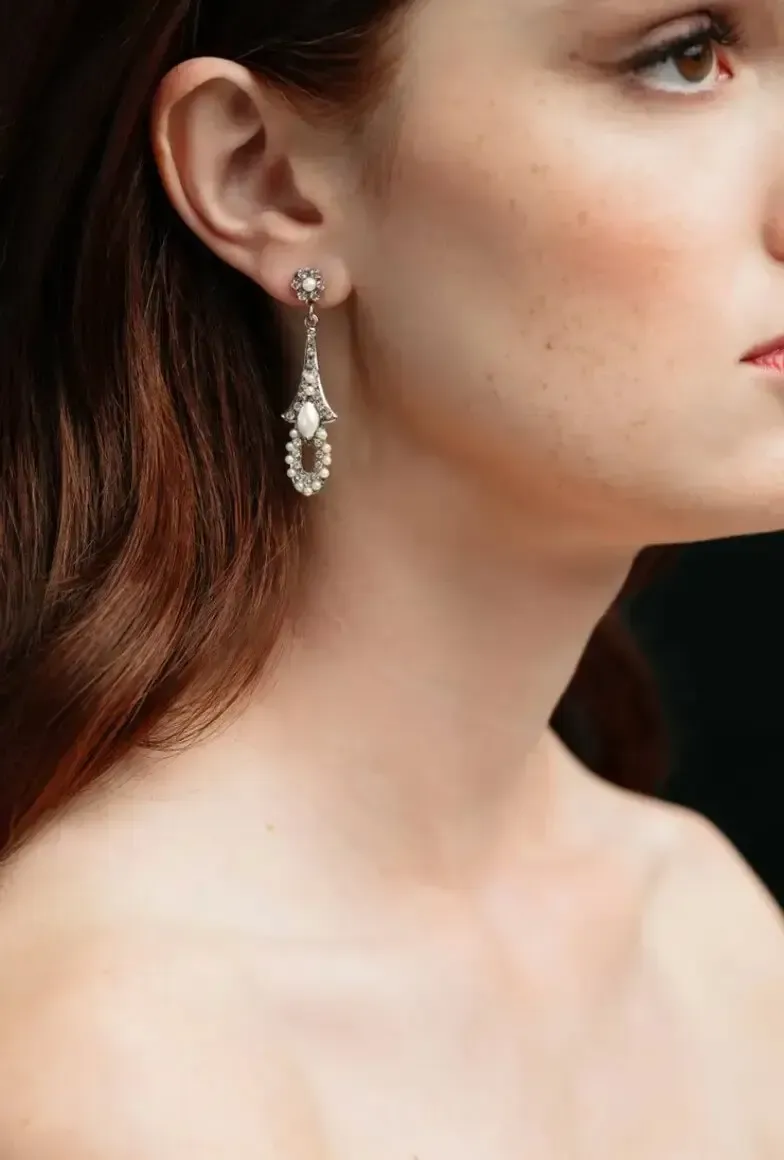 Woman wearing an ornate teardrop earring, side profile. Red hair, pale skin, dark background.