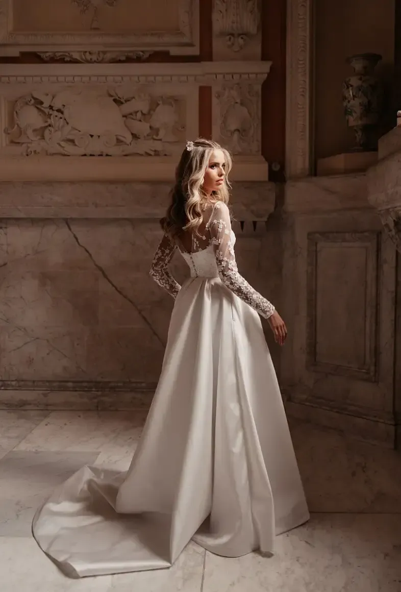 Woman in white wedding dress with long train, turned, looking over her shoulder in marble hallway.