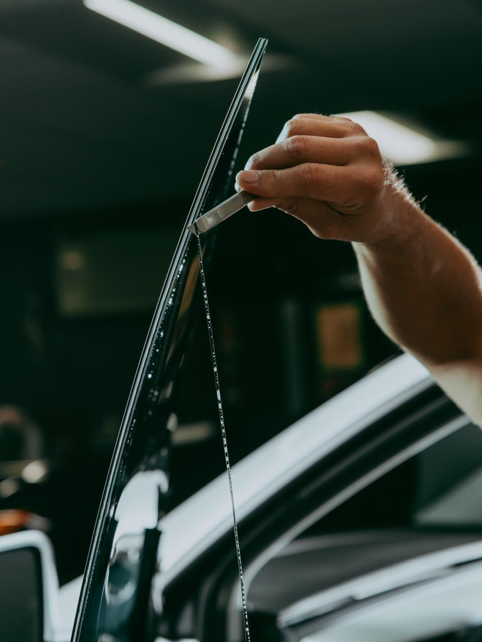 Person applying tint to a car window with a tool in a garage.