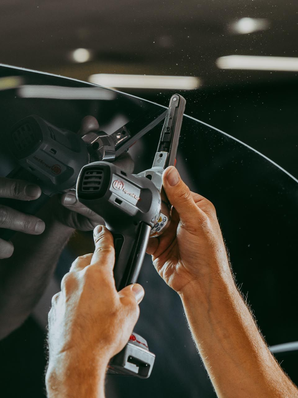 Person using a handheld tool, likely a heat gun, on curved glass in an auto shop.