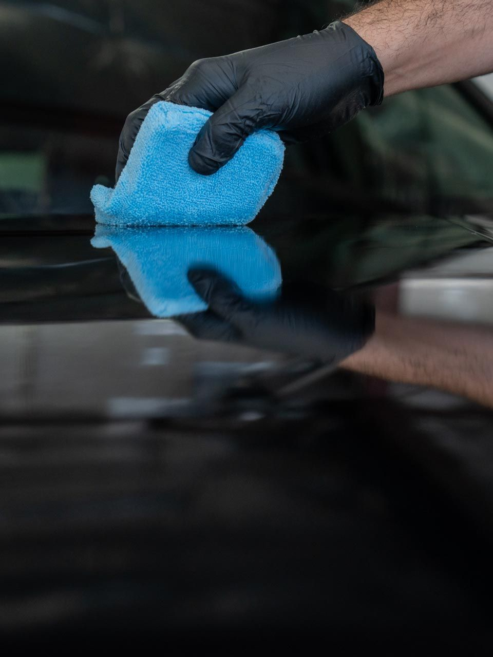 A person wearing black gloves is polishing a black car