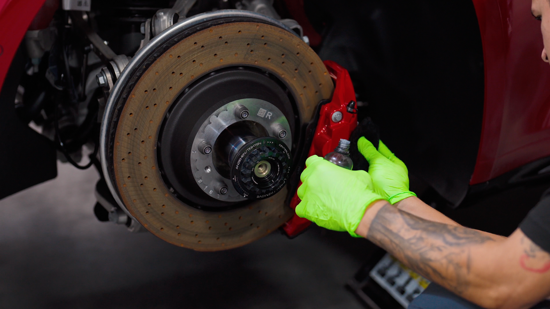 Mechanic in gloves working on a car's red brake caliper and rotor.