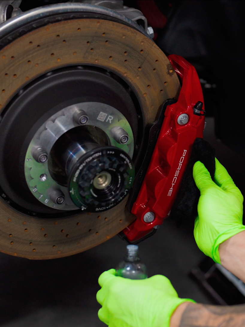 Person wearing green gloves working on a red brake caliper and rusty brake rotor.