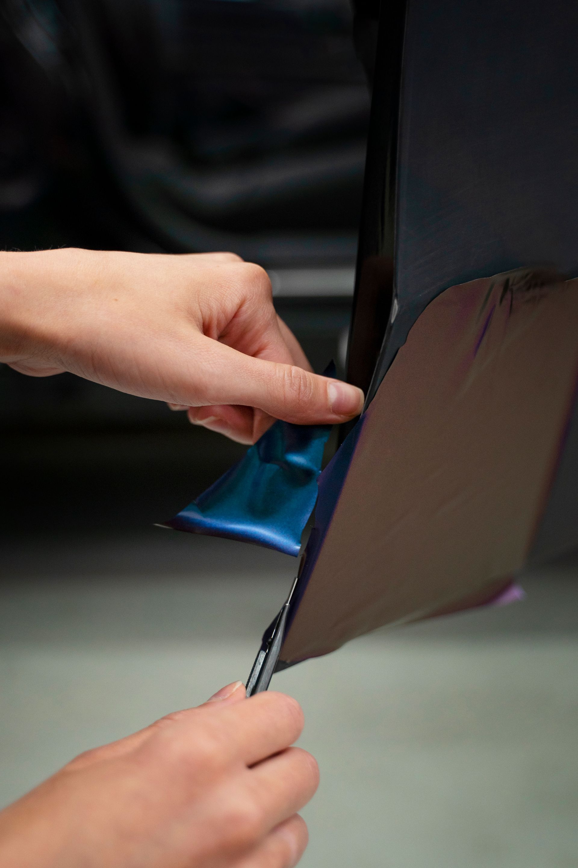 Hands peeling dark blue car wrap from a vehicle's side.