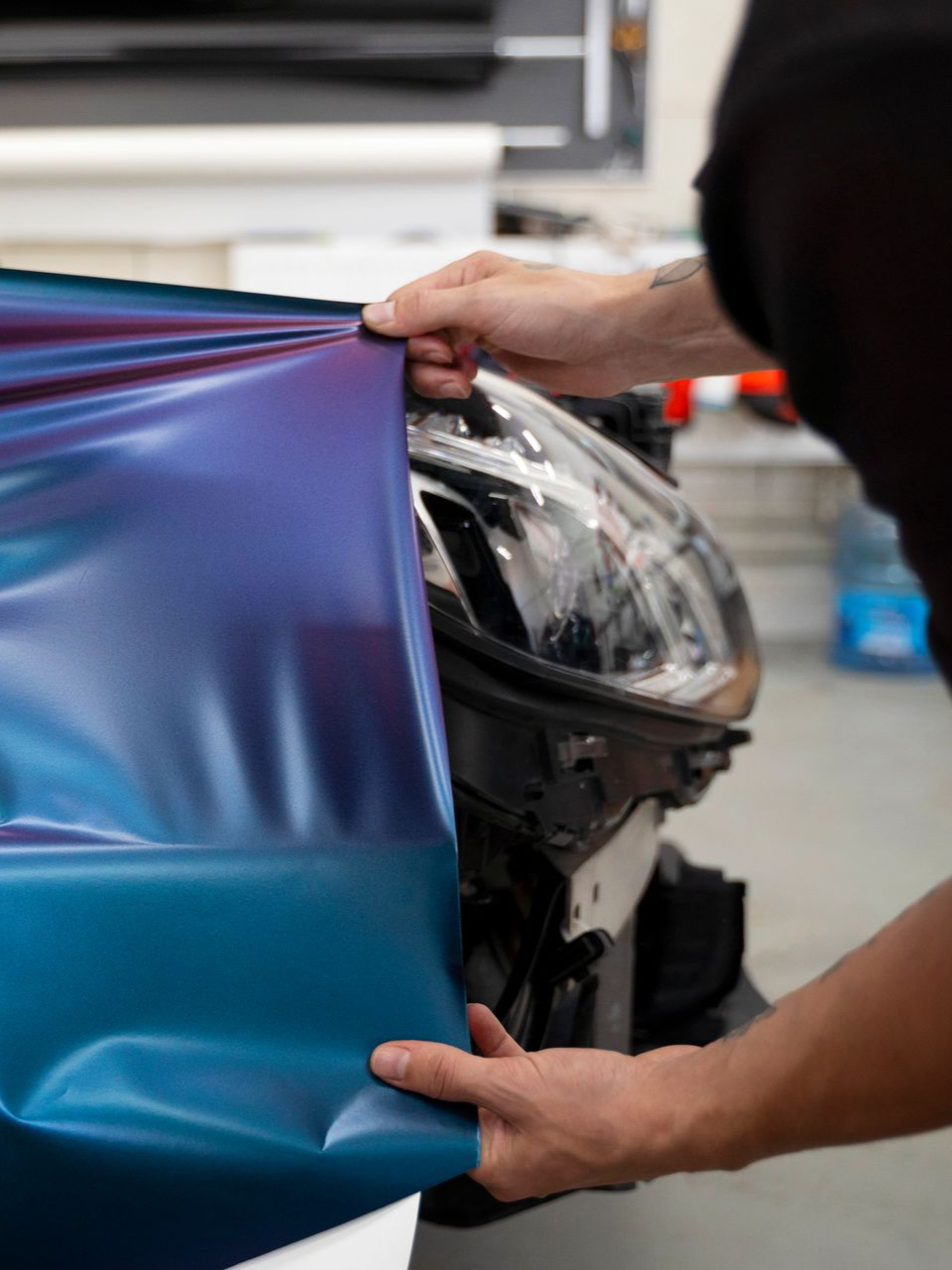Person applying iridescent blue vinyl wrap to a car headlight.