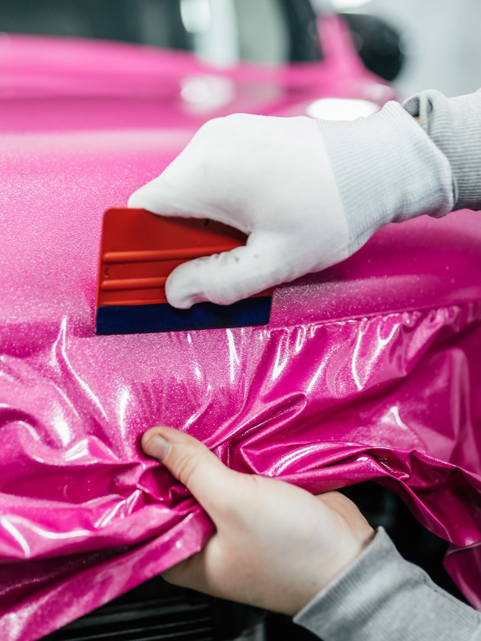 Person in white gloves smoothing pink glitter car wrap with a squeegee.