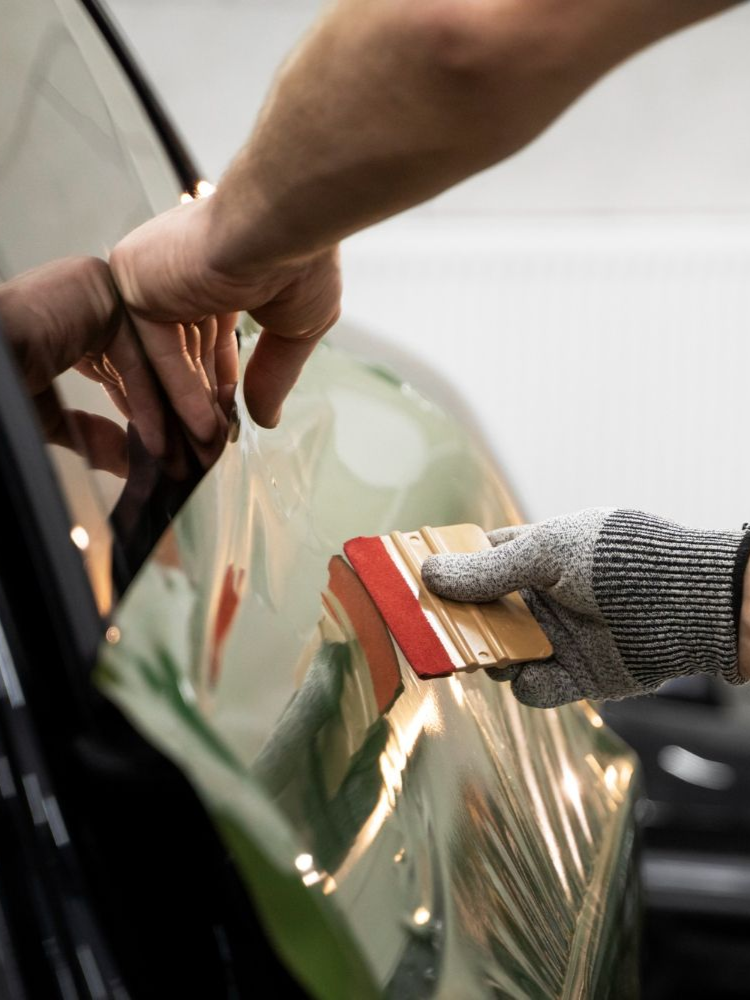 Person applying tint to a car window with a squeegee and wearing a glove.