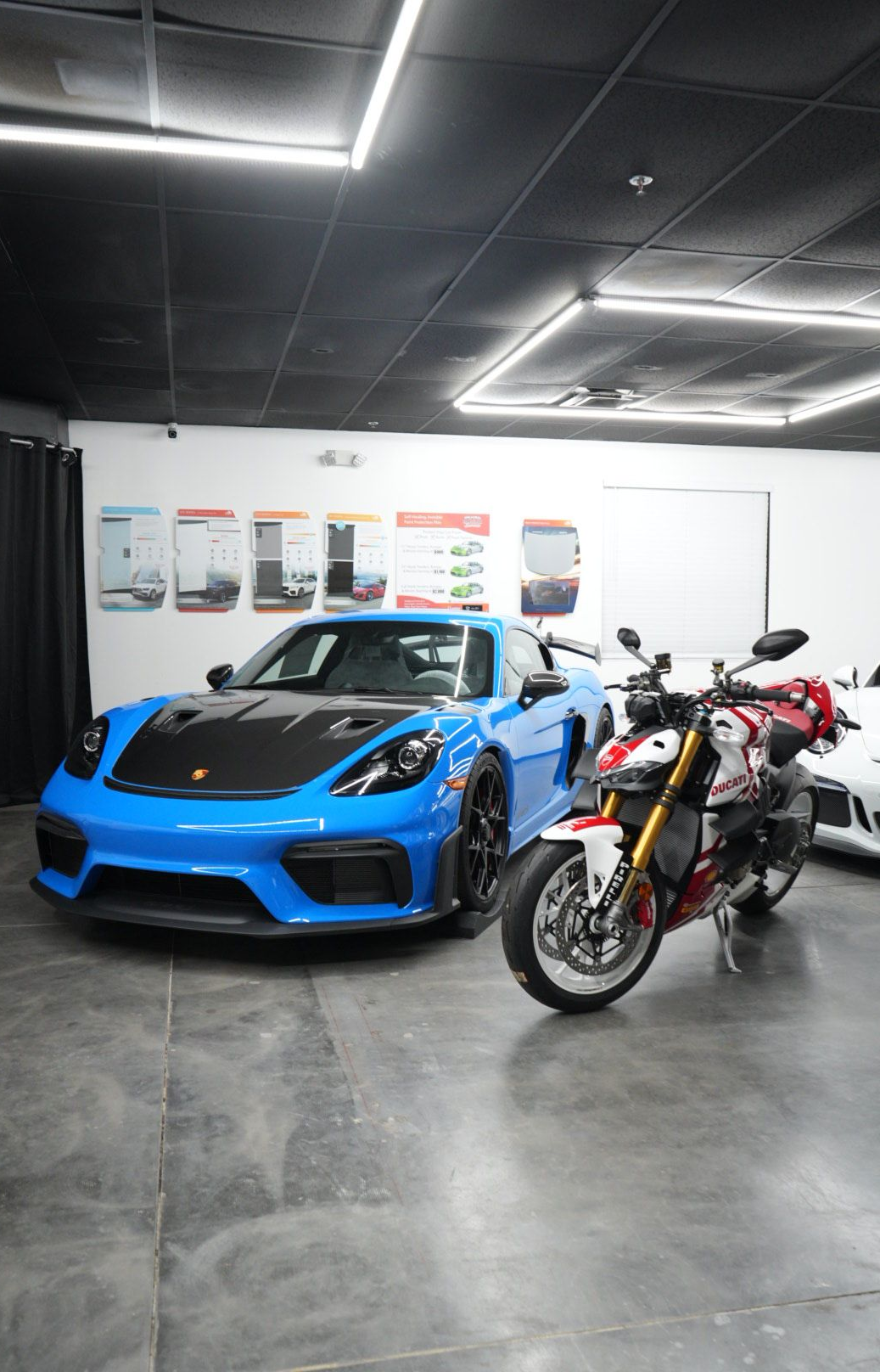 Blue Porsche and red motorcycle inside a showroom. Dark ceiling with bright lights.