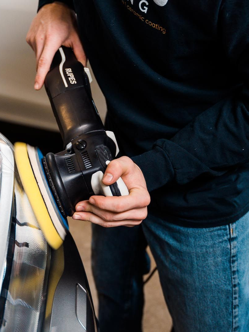 Person polishing car with a black and white electric buffer.