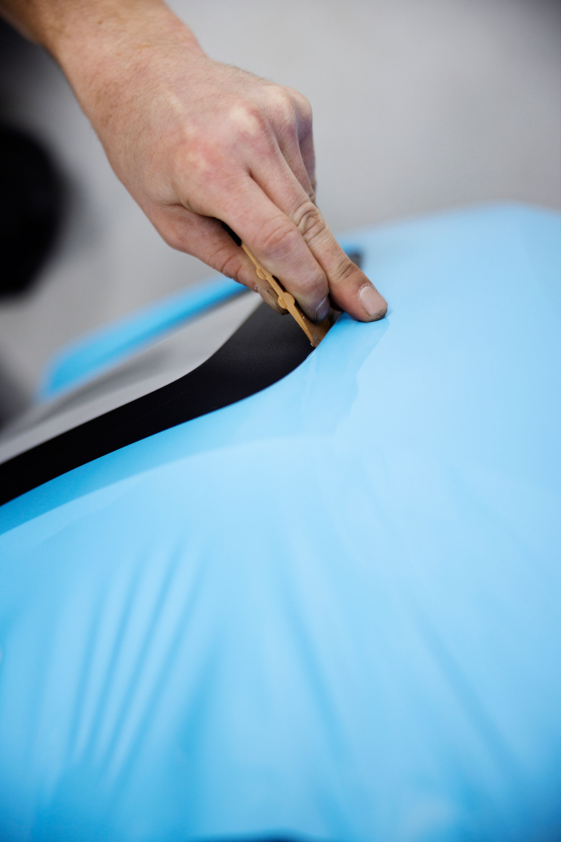 Person using a knife to trim blue vinyl wrapping on a car.