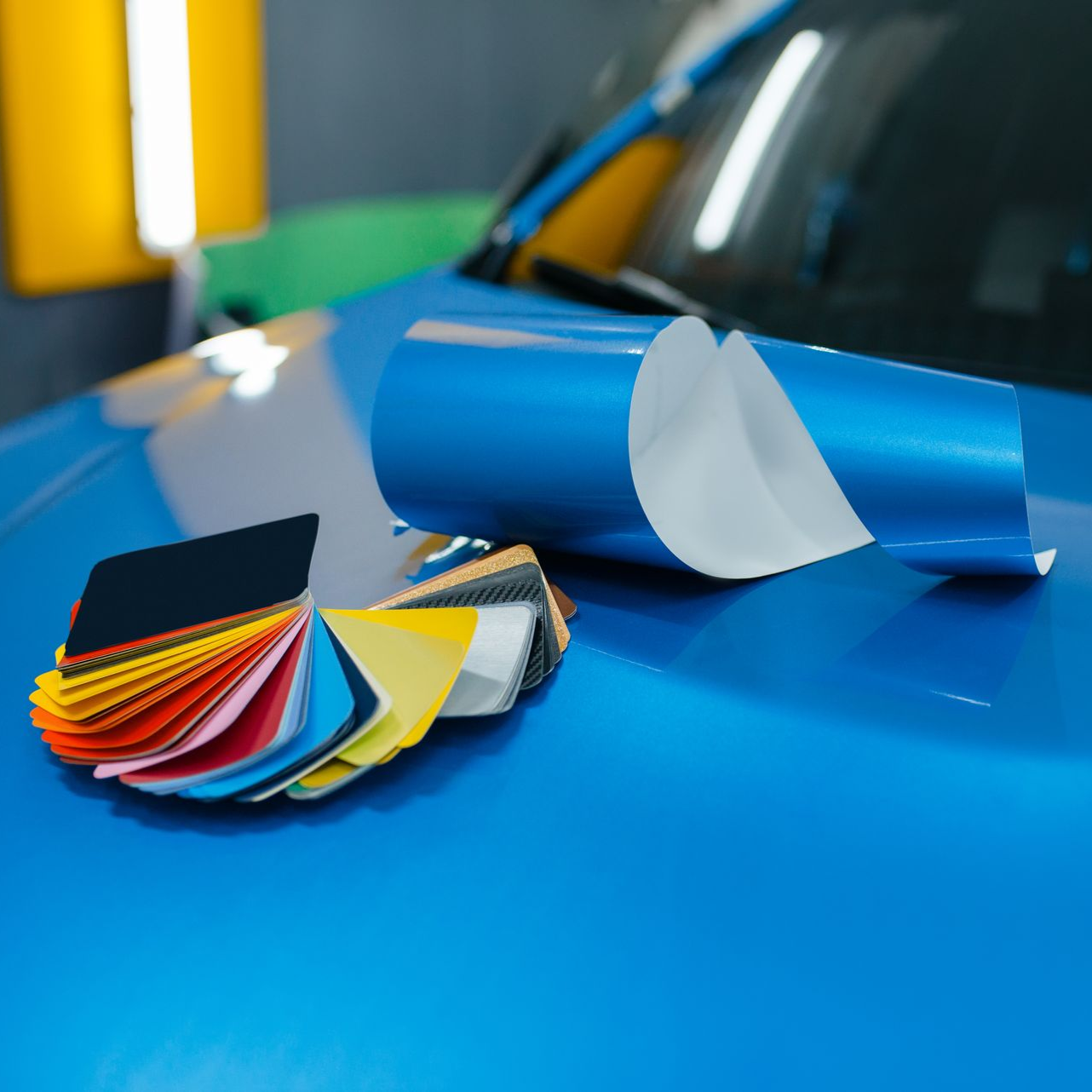 Blue car with color swatches and vinyl wrap roll for car customization.