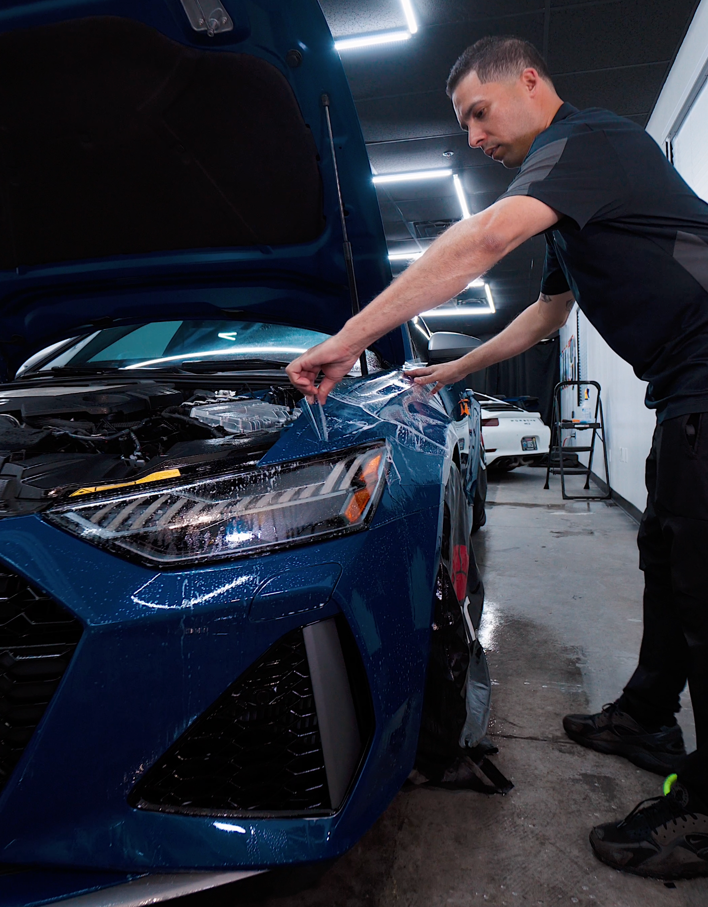 A man applying a protective film to a blue car in a garage.