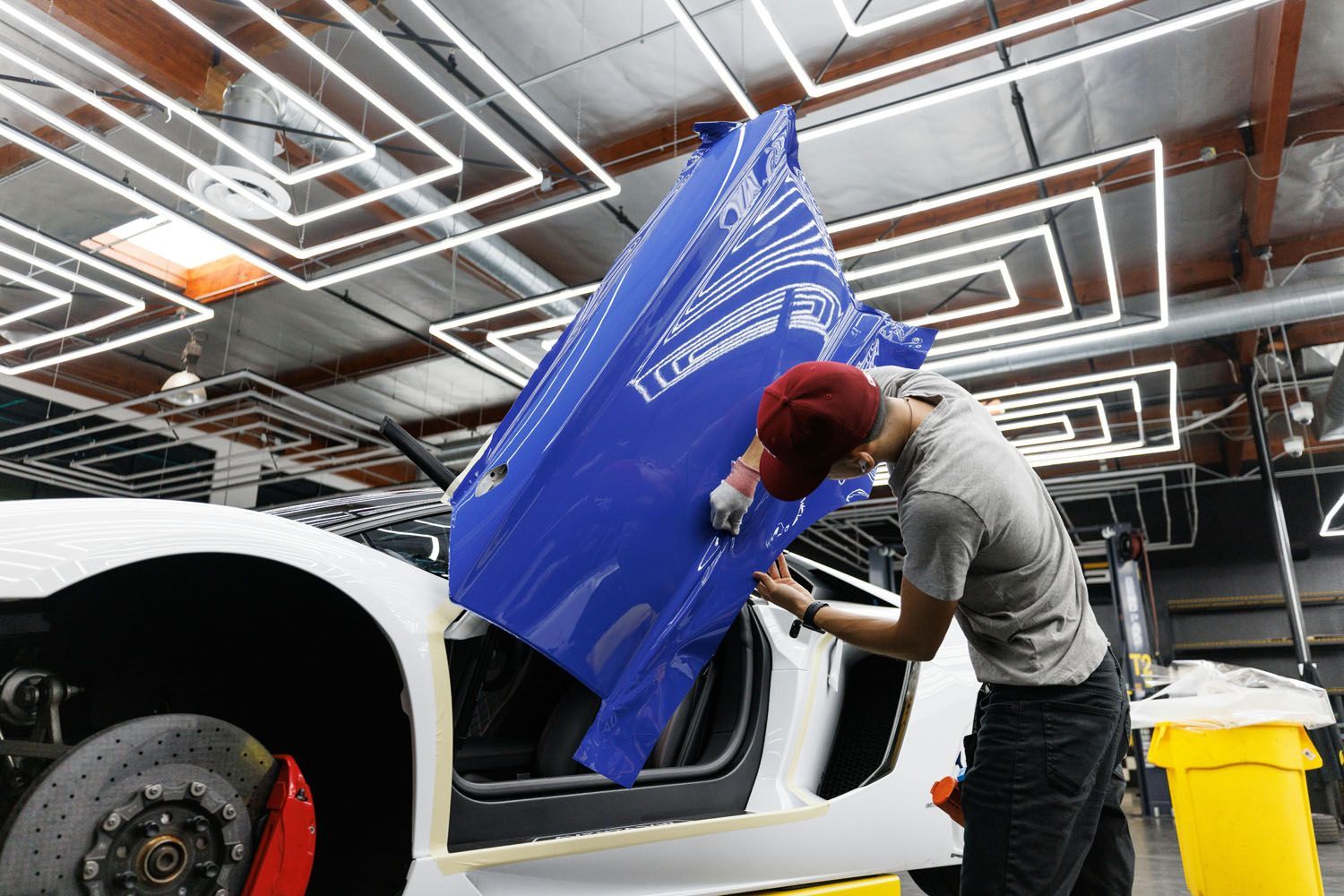 A man applying blue vinyl to a white Lamborghini door in a well-lit garage.
