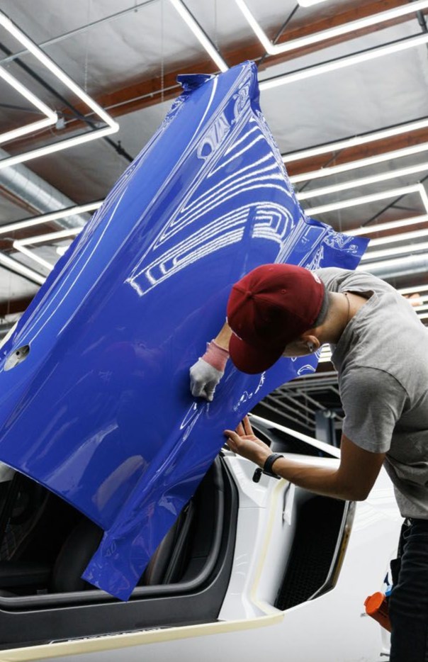 Person applying blue vinyl wrap to a car door in a brightly lit garage.