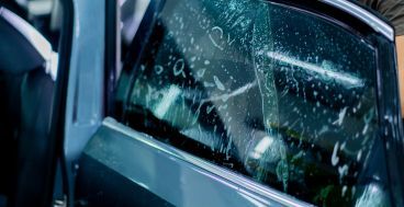 Applying tinted film to a car window, visible moisture, dark exterior, and hands working.