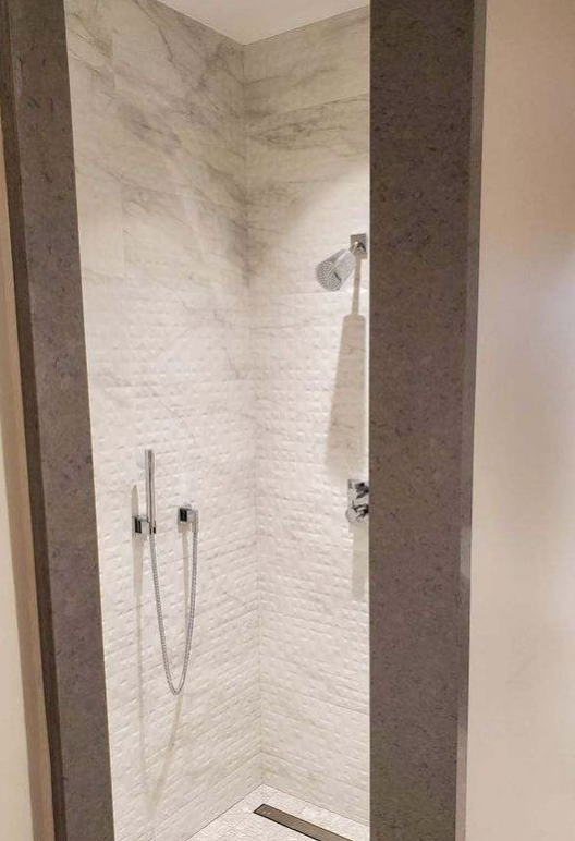There is a shower in the bathroom with a marble wall.
