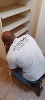 A man in a white shirt is kneeling down in front of a shelf.