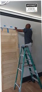 A man is standing on a ladder measuring a wooden door.