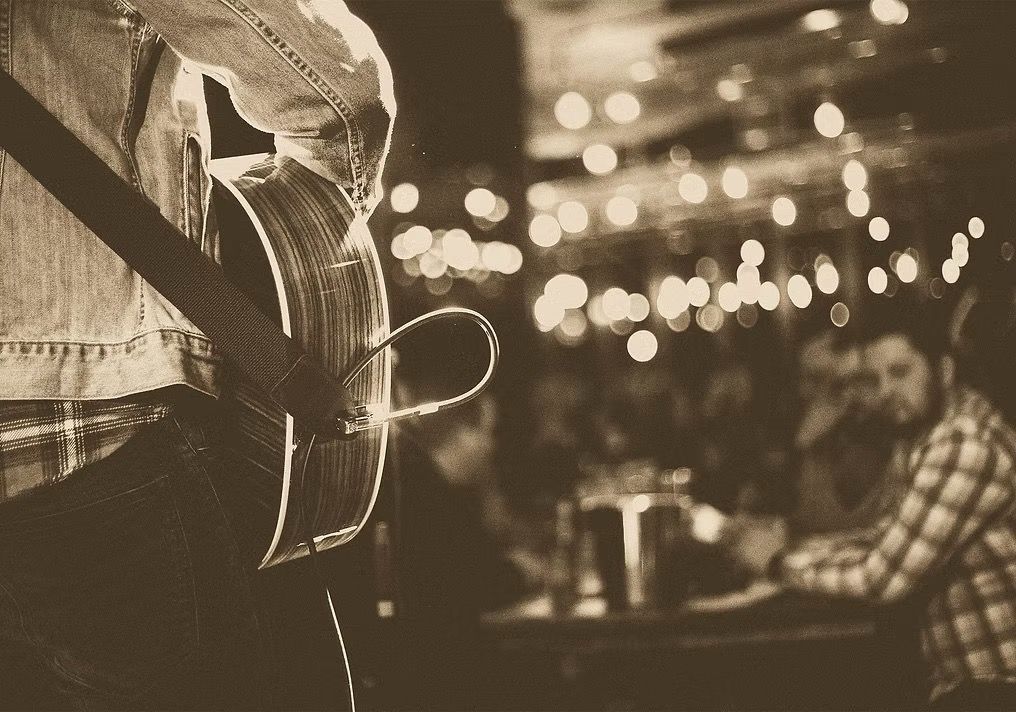 A man is playing an acoustic guitar in front of a crowd.