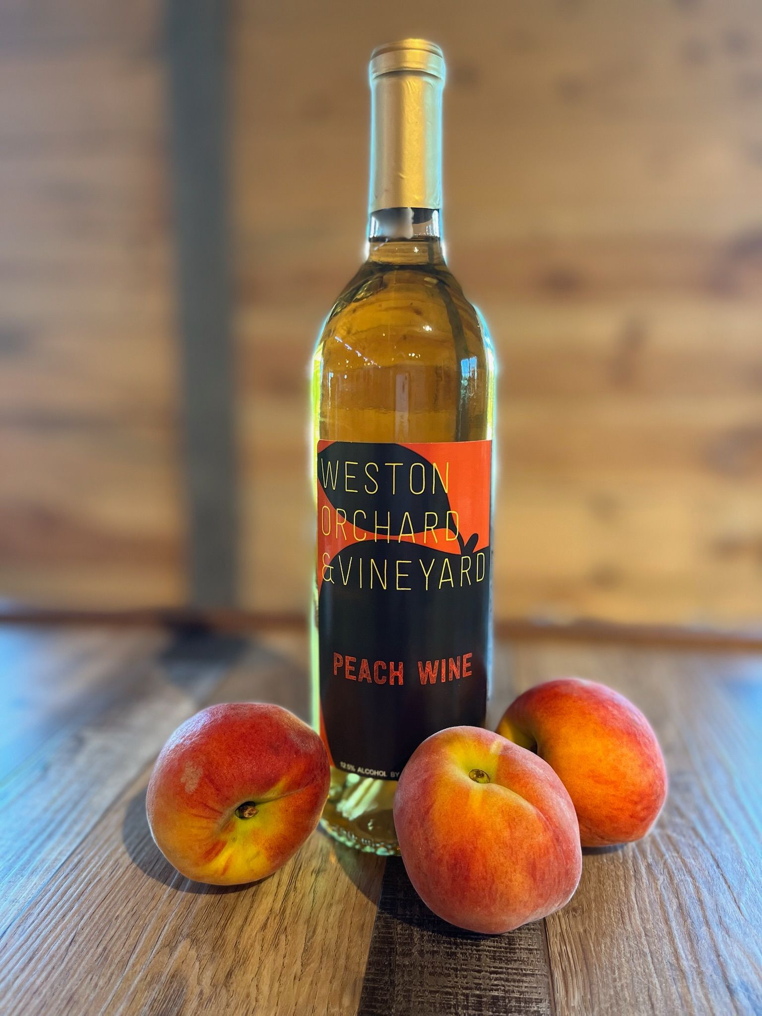 A bottle of peach wine is sitting on a wooden table next to two peaches.