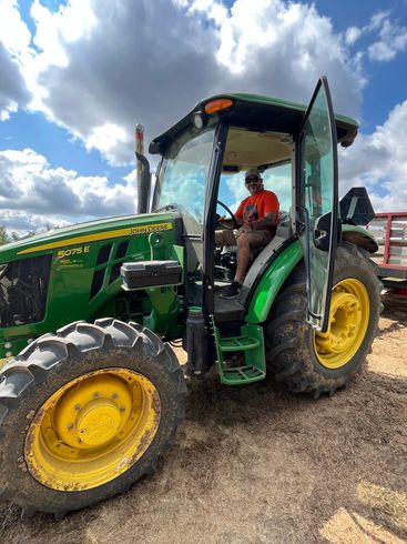 A man is sitting in the driver 's seat of a green john deere tractor.