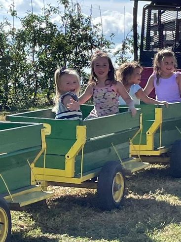 A group of young girls are riding in a green and yellow wagon.