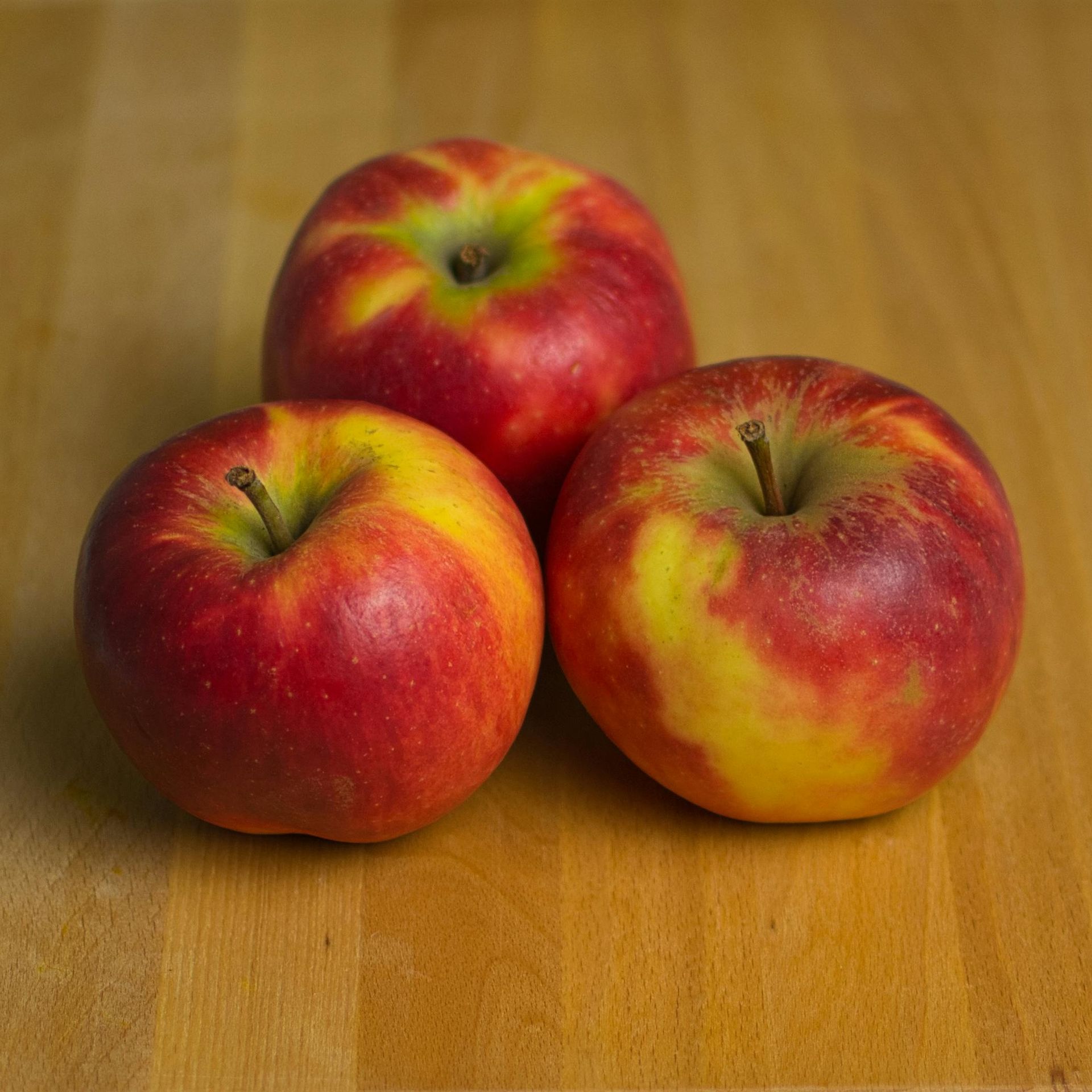 Three apples are sitting on a wooden table.