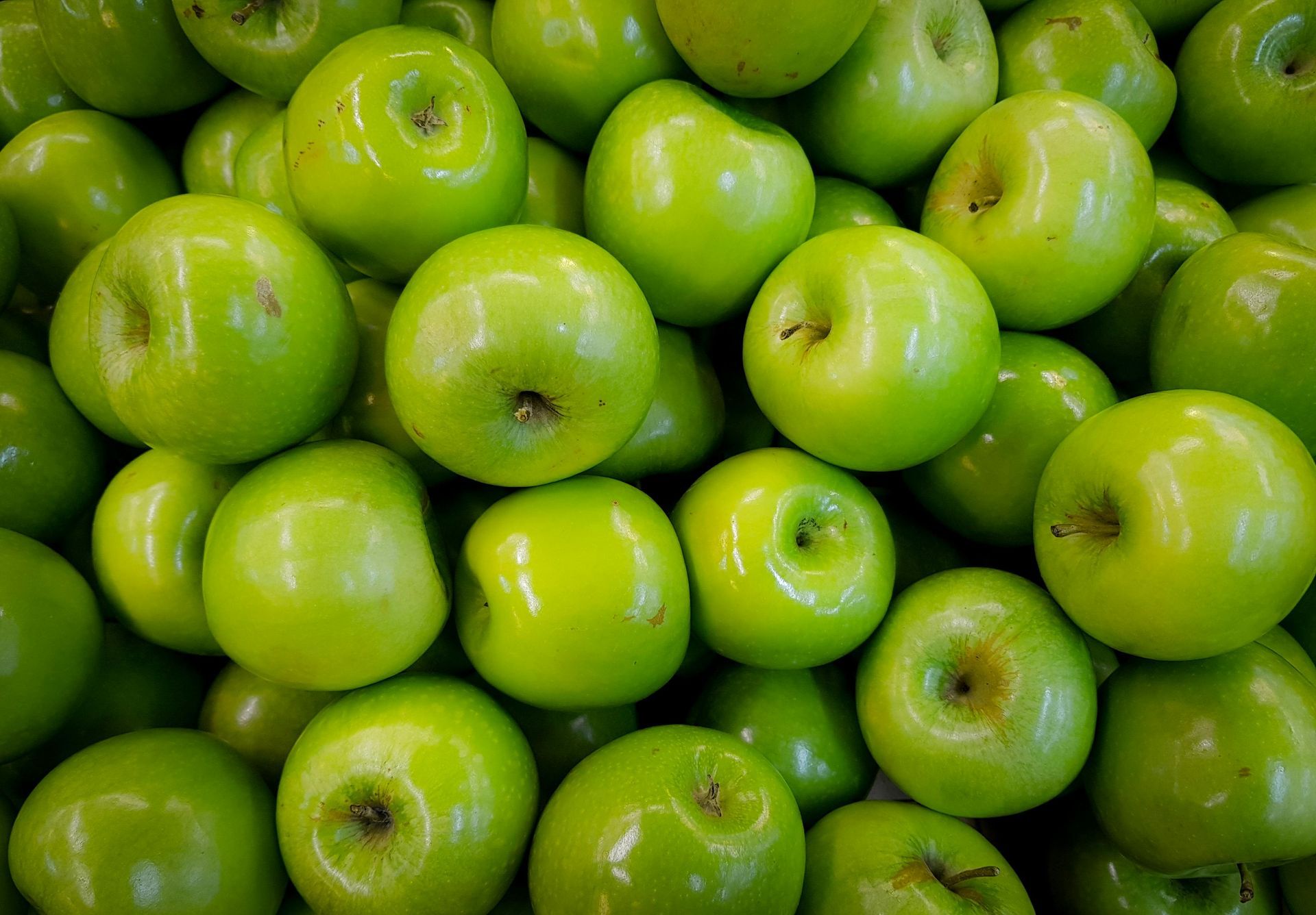 A pile of green apples sitting on top of each other on a table.
