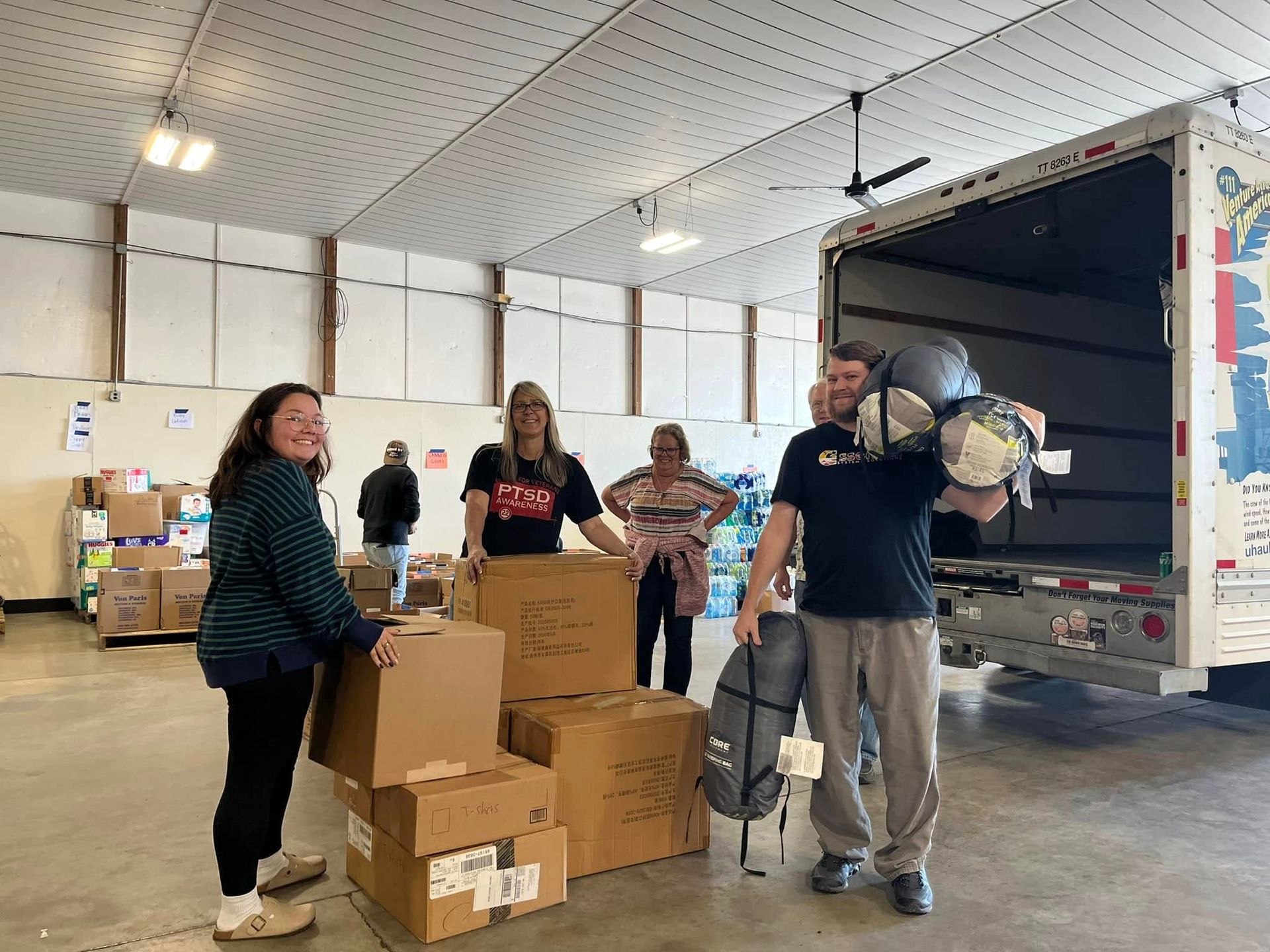 People loading boxes and gear into a truck, likely for donation; inside a warehouse.