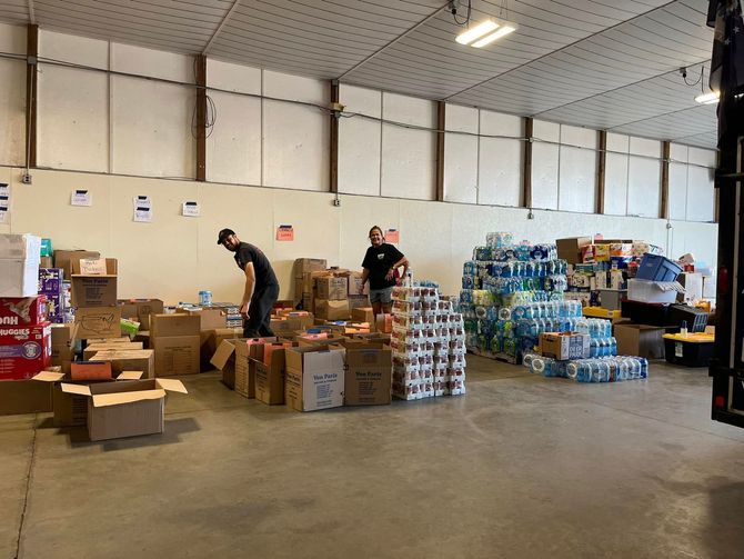 Warehouse interior with two people sorting boxes and pallets of water bottles.