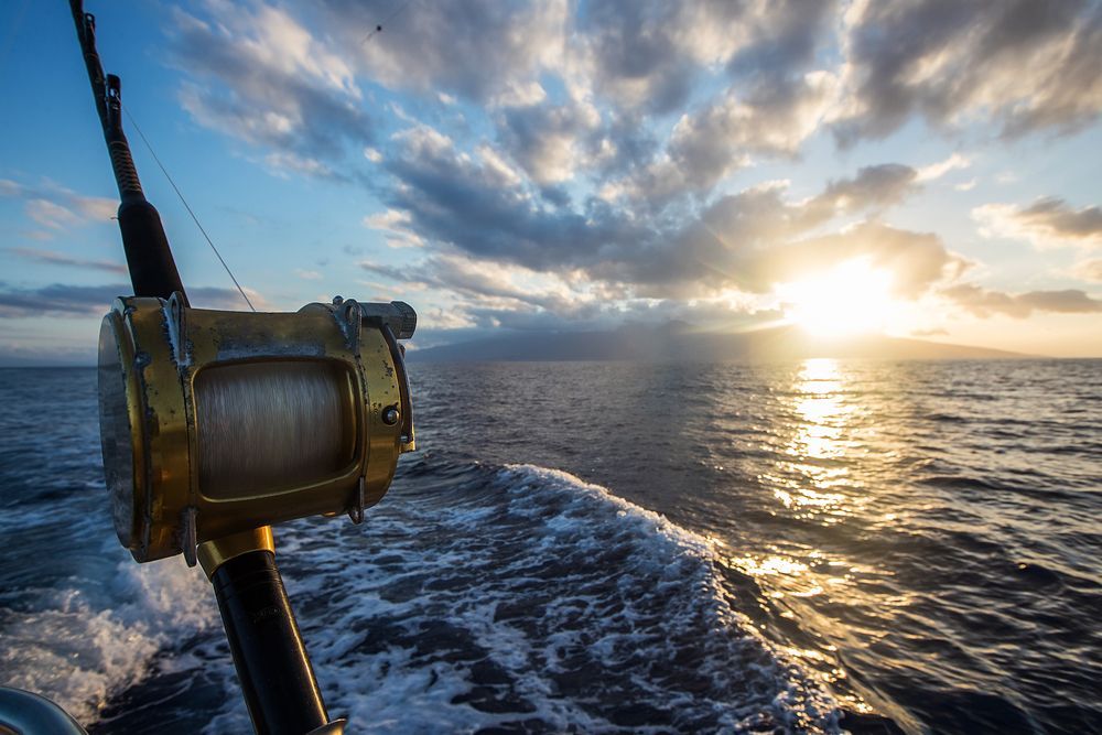 A fishing rod is being pulled by a boat in the ocean at sunset.