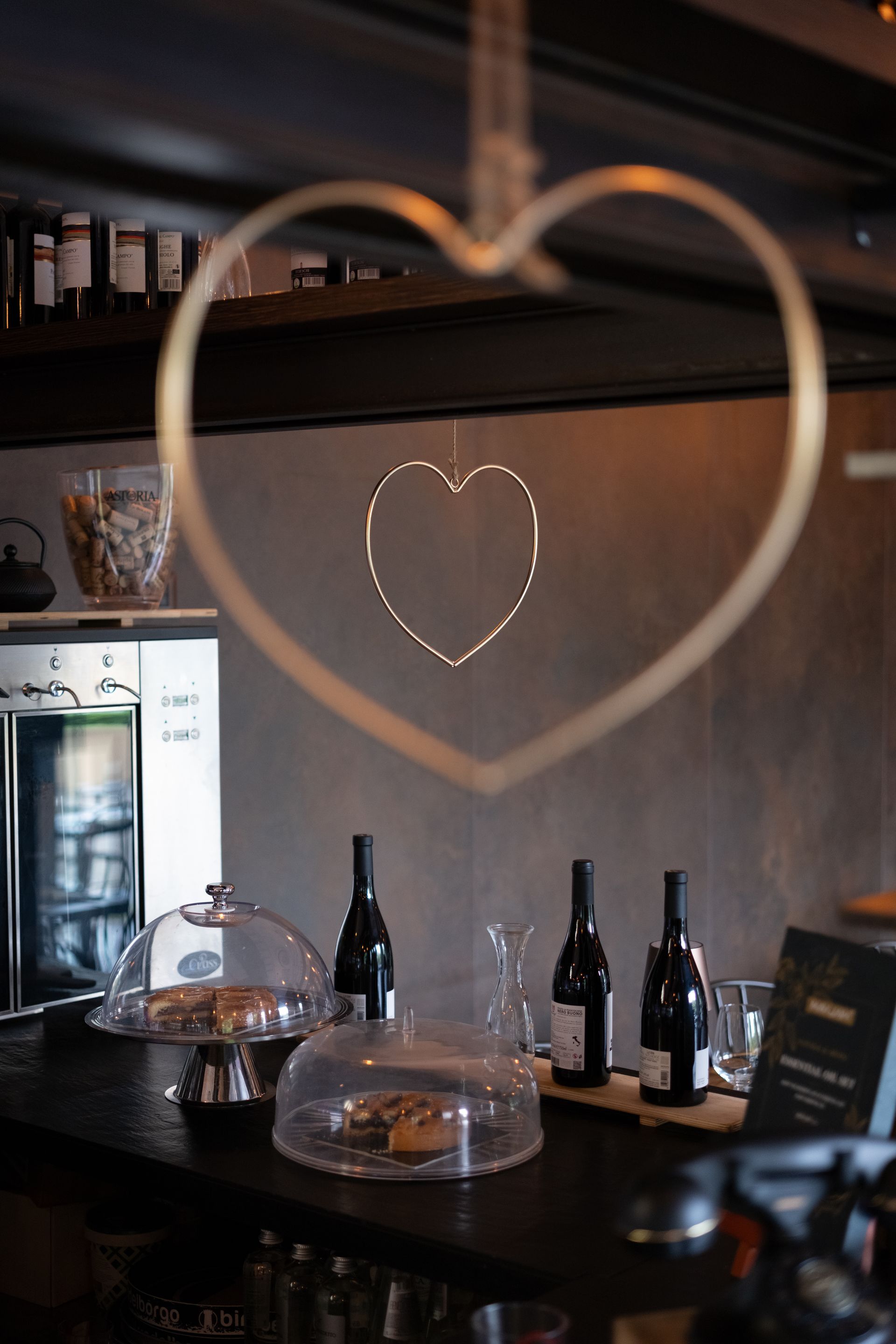 Decorazione a forma di cuore appesa davanti a un bar con bottiglie di vino, torte e altri oggetti esposti.