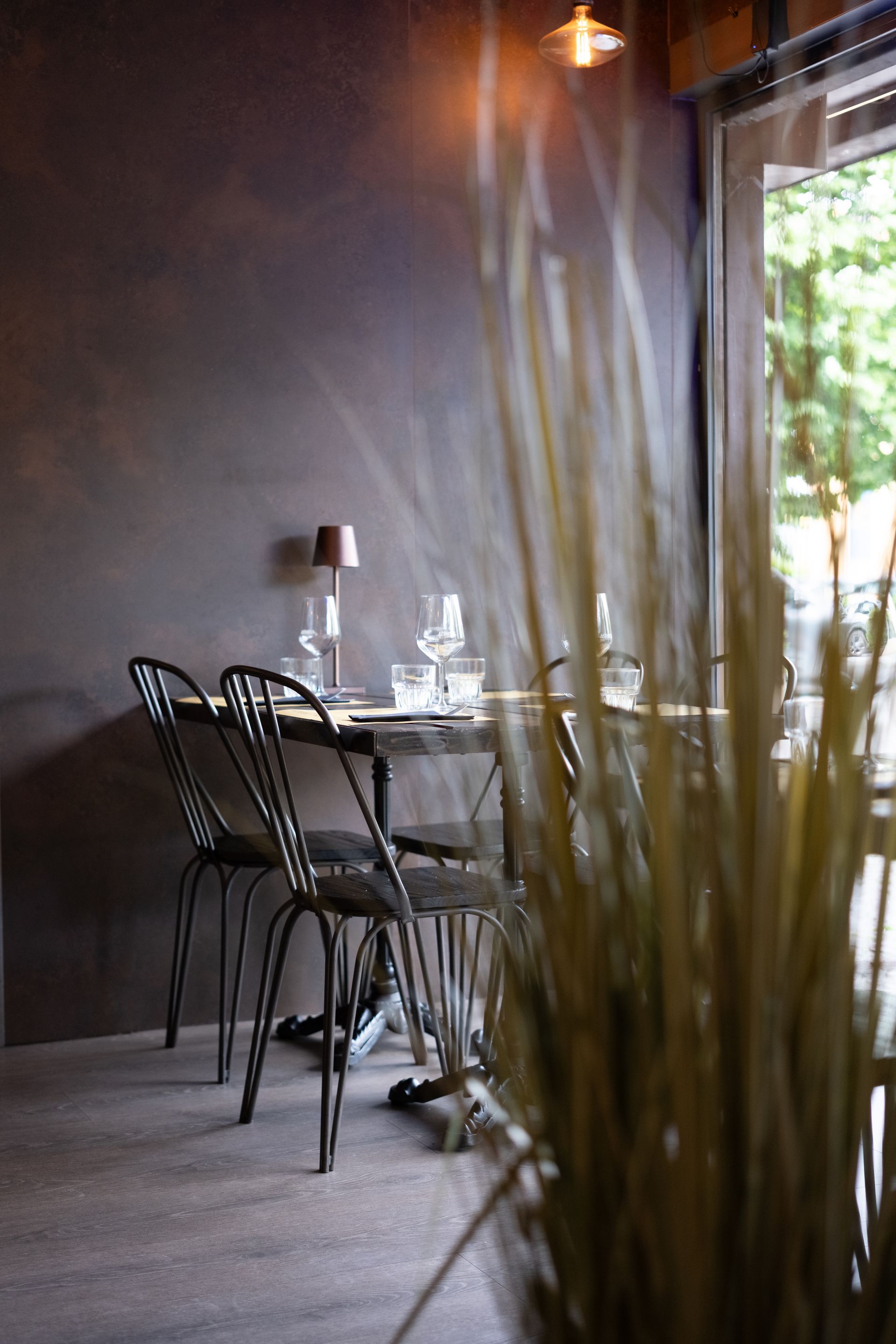 Tavolo apparecchiato per due, con sedie, vicino a una finestra, illuminato da una piccola lampada, all'interno di un ristorante.