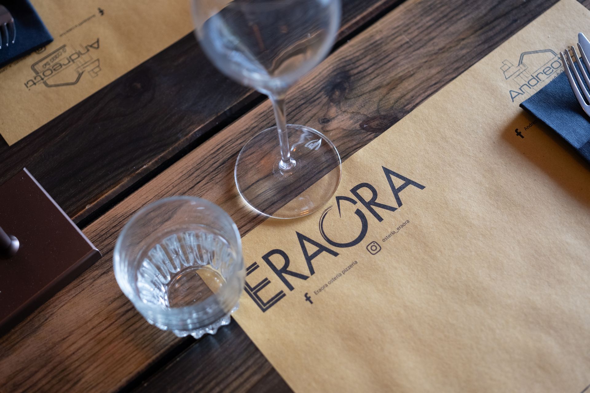 Apparecchiatura da tavola con bicchiere da vino e bicchiere da acqua, con tovaglietta con la scritta "ERAGRA".