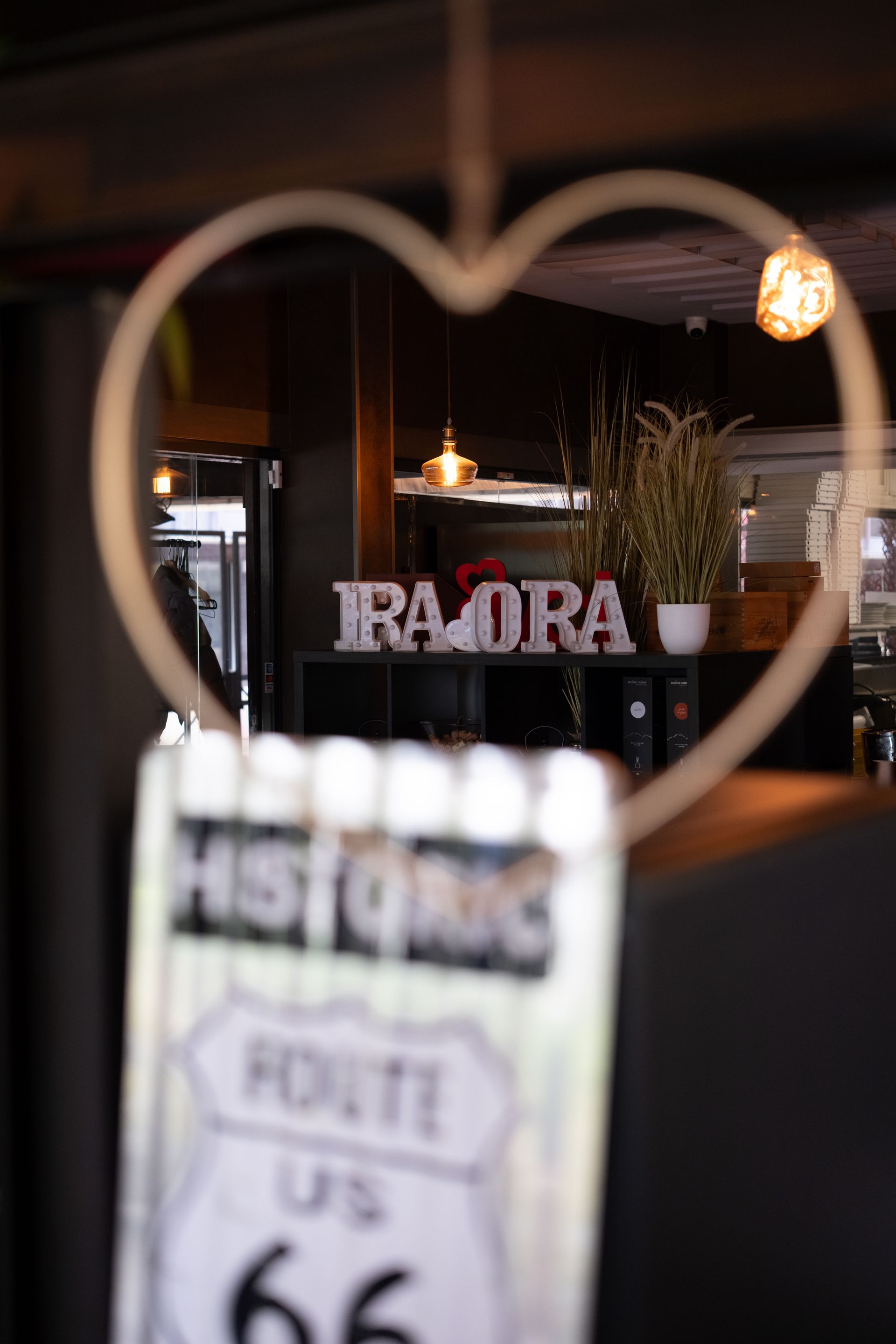 Una decorazione a forma di cuore incornicia un cartello con la scritta "IRAORA" in un ristorante. Sotto c'è un cartello della Route 66.