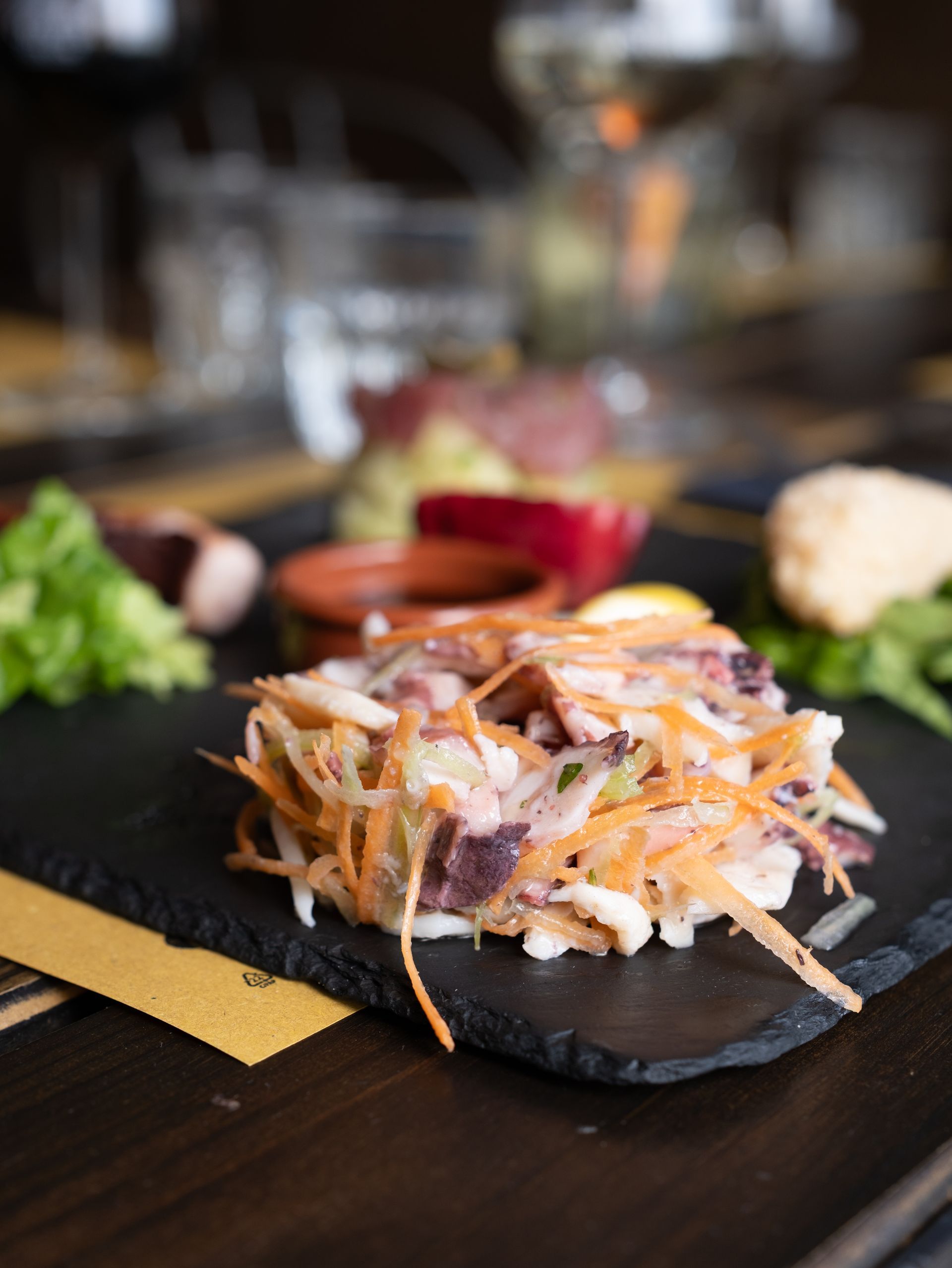 Insalata di cavolo e altri antipasti su un piatto scuro, disposti su un tavolo di legno.