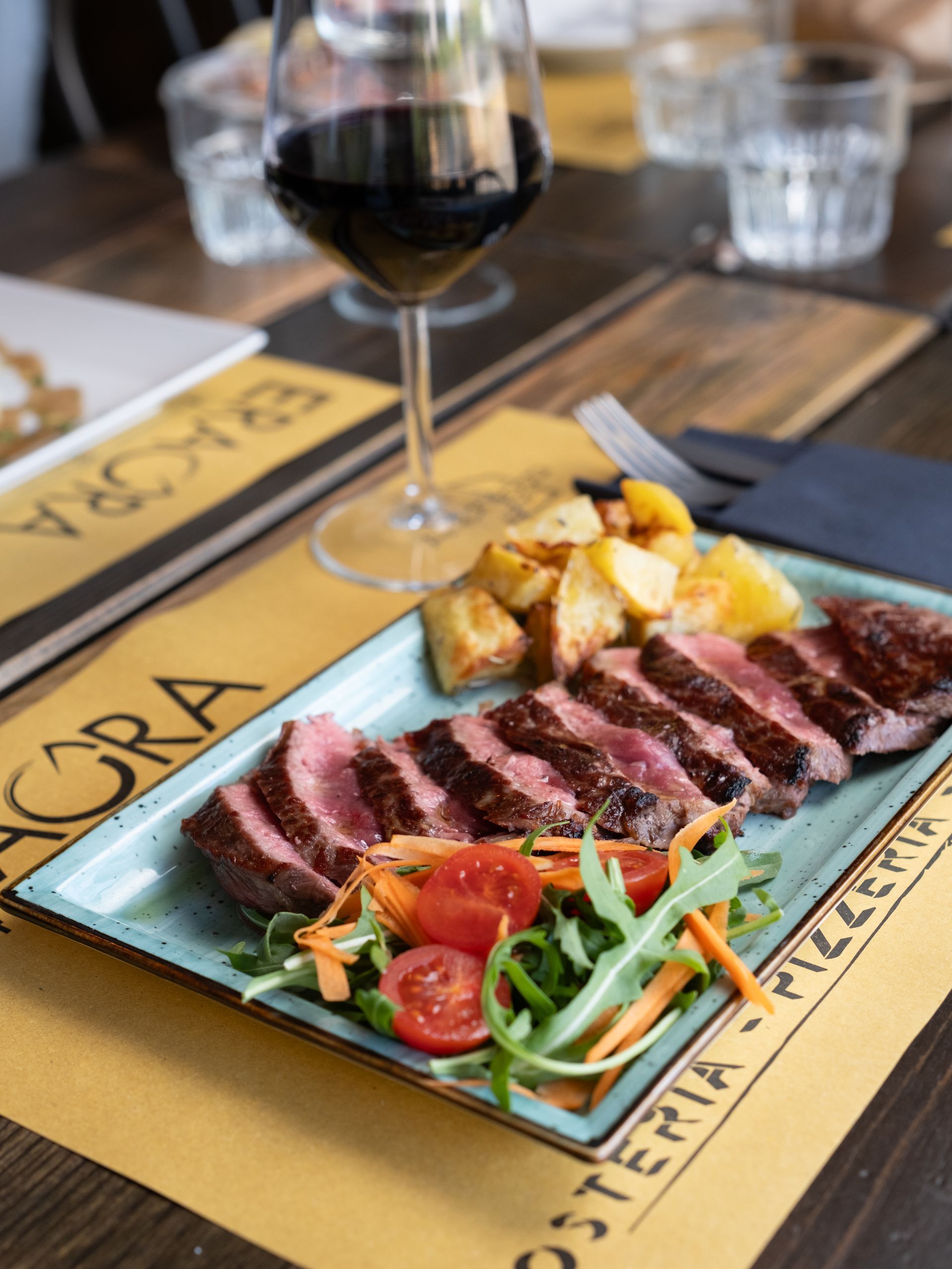 Bistecca tagliata con patate arrosto, insalata e un bicchiere di vino rosso sul tavolo di un ristorante.